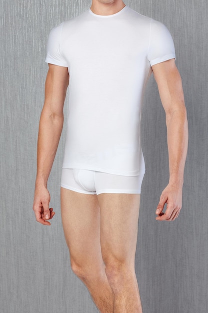 Modèle masculin portant un t-shirt blanc et une culotte devant un fond gris. Sous-vêtements pour hommes.