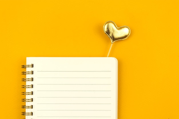 Modèle de message d'amour de composition à plat avec bloc-notes sur une table jaune et un coeur jaune, photo vue de dessus avec espace de copie