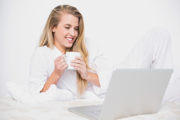 Modèle mignon souriant tenant le café allongé sur le lit douillet