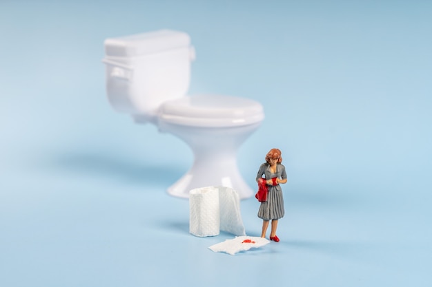 Un modèle miniature d'une femme se tient près d'une toilette jouet avec du papier toilette avec du sang