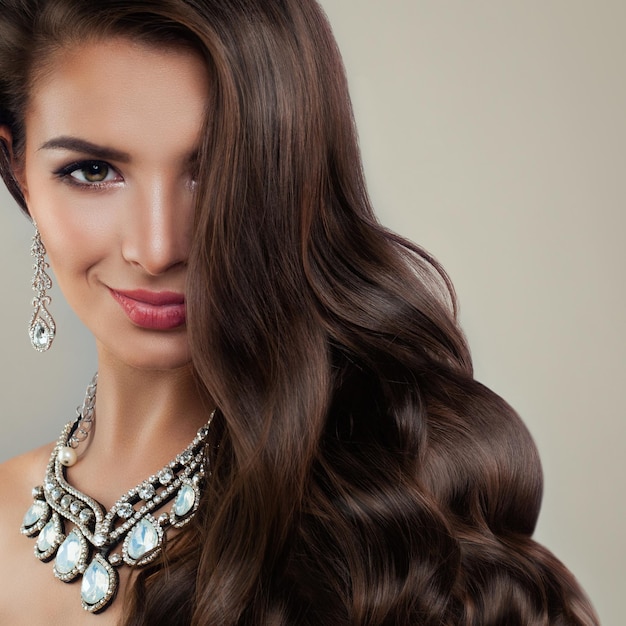 Modèle de mode femme parfaite avec des boucles d'oreilles en diamant et des colliers de bijoux. Belle dame avec maquillage et cheveux bouclés