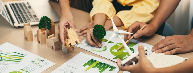 Modèle de moulin à vent représenté utilisant une énergie renouvelable placée lors de la présentation d'une entreprise verte sur une table avec un bloc de bois et un document environnemental dispersé autour de la délimitation en gros plan