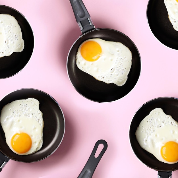 Modèle de nourriture créative avec des œufs frits sur des casseroles sur fond rose Vue de dessus Modèle créatif dans un style minimal Mise à plat Culture carrée