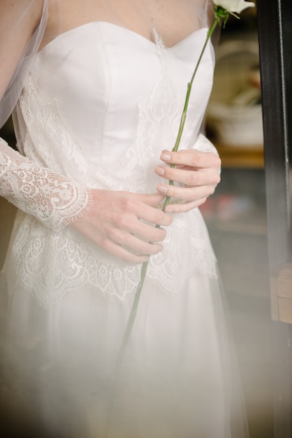 Modèle posant dans une robe de mariée blanche tient une fleur dans sa main