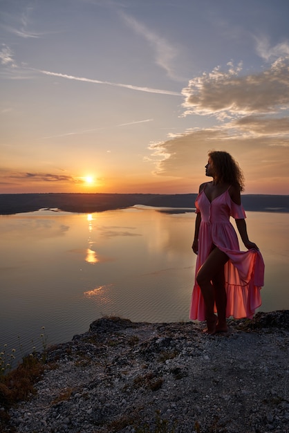 Modèle en robe longue posant sur fond de coucher de soleil.