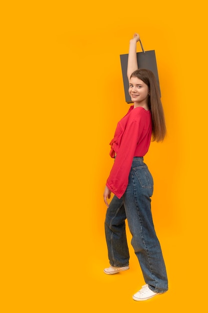 Modèle souriant dans les vêtements de jeunesse contient des sacs en papier noir Fond jaune Black Friday Shopping concept Cadre vertical