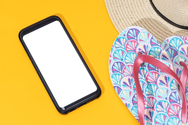 Photo modèle de téléphone intelligent avec des tongs blancs à écran blanc et un chapeau sur fond jaune concept de voyage d'été