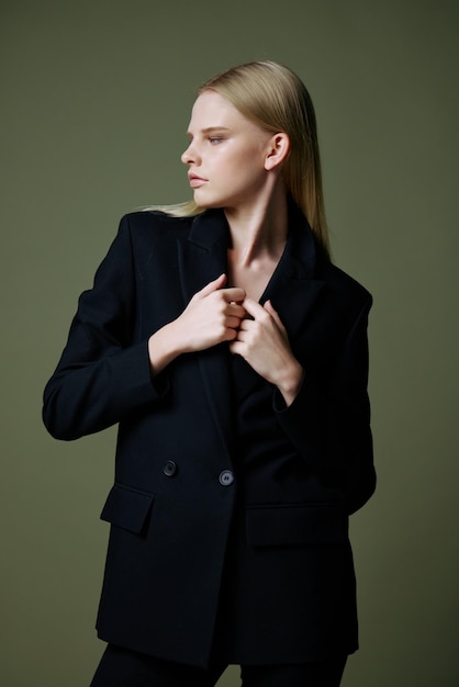 Le modèle tient la veste par le col tout en posant sur un fond vert dans le studio Photo conceptuelle pour les marques de vêtements Offre cool pour les costumes à la mode