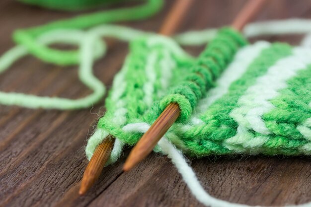 Modèle de tricot de fil vert sur des aiguilles en bois et écheveau sur un fond en bois