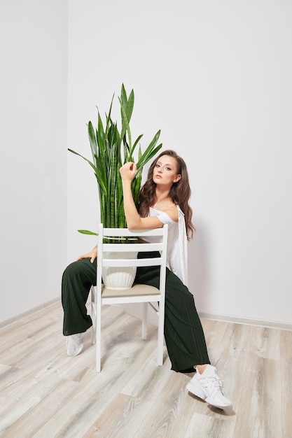 Modèle en vêtements élégants assis sur une chaise en bois avec une plante verte