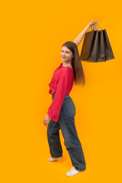 Modèle en vêtements de jeunesse contient des sacs en papier noir Prise de vue en studio sur fond jaune Black Friday Shopping concept Cadre vertical