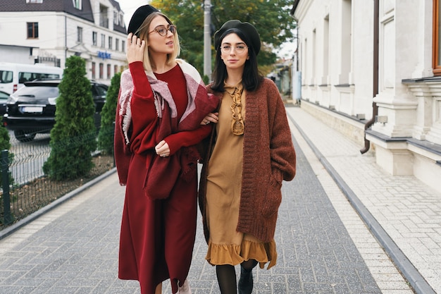 Modèles féminins à la mode sans soucis dans des vêtements et des lunettes d'automne élégants. Jeunes filles de la mode dans des vêtements élégants en laine tissée et des chapeaux sur la rue de la ville urbaine, portrait d'automne.