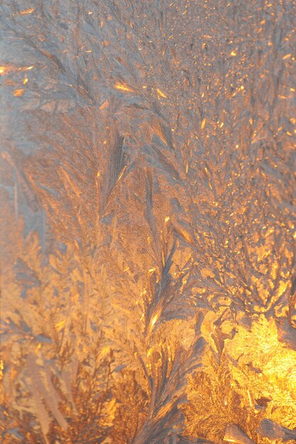 Modèles de glace et lumière du soleil du soir sur le verre d'hiver