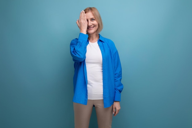 Modeste femme mûre aux cheveux blonds dans une chemise décontractée sur fond bleu avec espace de copie