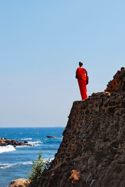 Le moine bouddhiste se dresse sur le rocher et regarde en mer, un navire y va, Sri Lanka