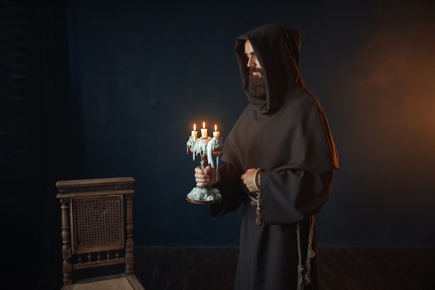 Moine médiéval en robe tient un chandelier dans les mains