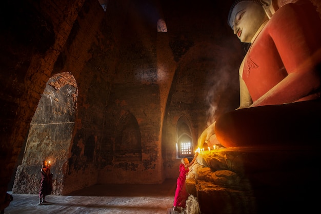 Moine priant une statue de Bouddha avec bougie