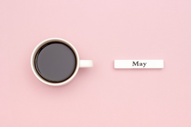 mois du mois de mai et tasse de café noir sur fond de papier rose pastel.