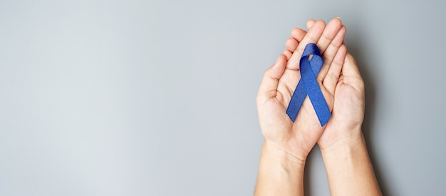 Mois de sensibilisation au cancer colorectal, homme tenant un ruban bleu foncé pour soutenir les personnes vivant et malades.