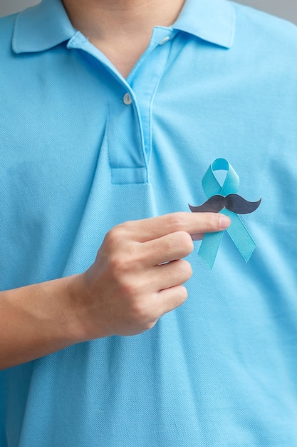 Photo mois de sensibilisation au cancer de la prostate de novembre, homme tenant un ruban bleu avec une moustache pour soutenir les personnes vivant et malades. soins de santé, hommes internationaux, père et concept de la journée mondiale du cancer