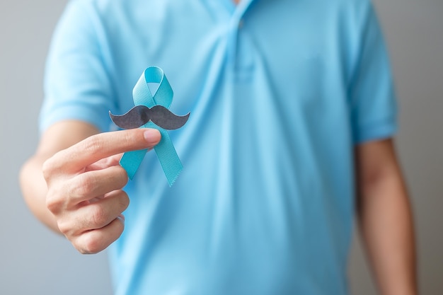 Mois de sensibilisation au cancer de la prostate de novembre, homme tenant un ruban bleu avec une moustache pour soutenir les personnes vivant et malades. Soins de santé, hommes internationaux, père et concept de la journée mondiale du cancer