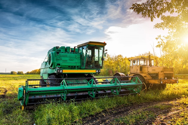 La moissonneuse-batteuse verte moderne et le tracteur robuste jaune sur le terrain agricole dans les rayons du soleil d'automne