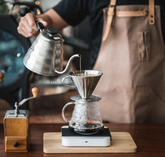 La moitié d'un barista versant du café dans un pot sur la table