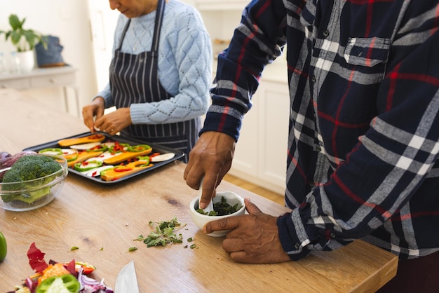 Photo la moitié d'un couple de personnes âgées diversifiées prépare un repas sain avec des légumes dans la cuisine