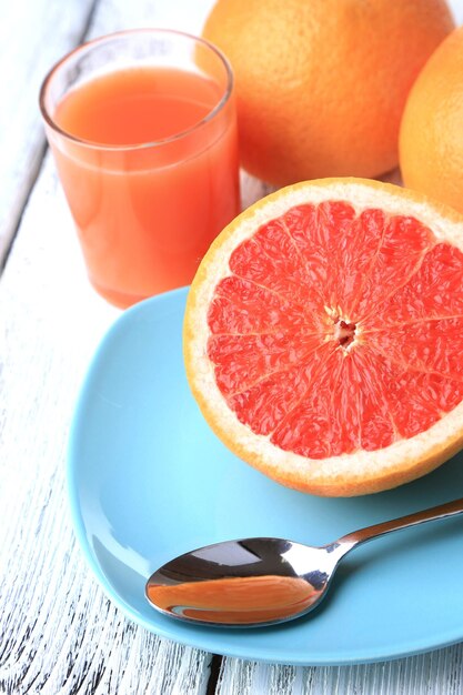 Photo la moitié du verre de pamplemousse de jus de fruits frais et une cuillère sur une assiette sur fond clair