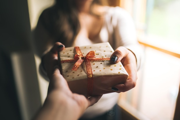 La moitié d'une femme donnant une boîte-cadeau à un ami contre la fenêtre