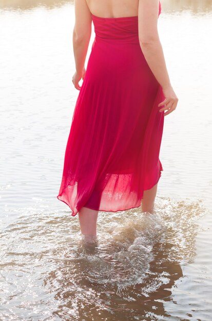 La moitié d'une femme en robe rouge pataugeant dans la mer