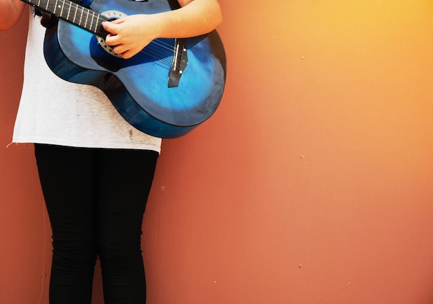 La moitié d'une fille jouant de la guitare contre un mur orange