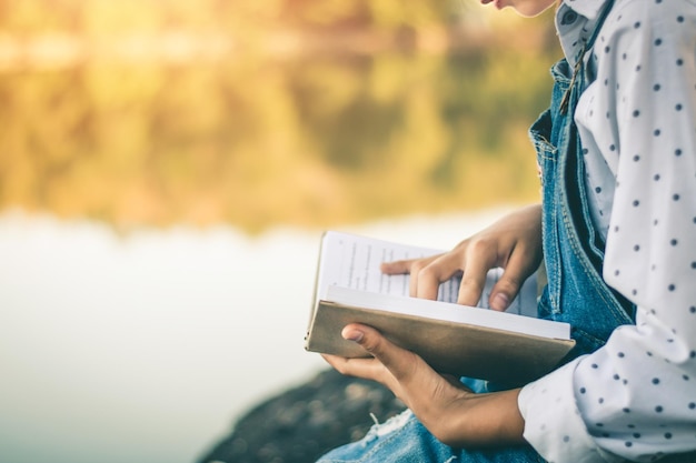 Photo la moitié d'une fille lisant un livre assise au bord d'un lac