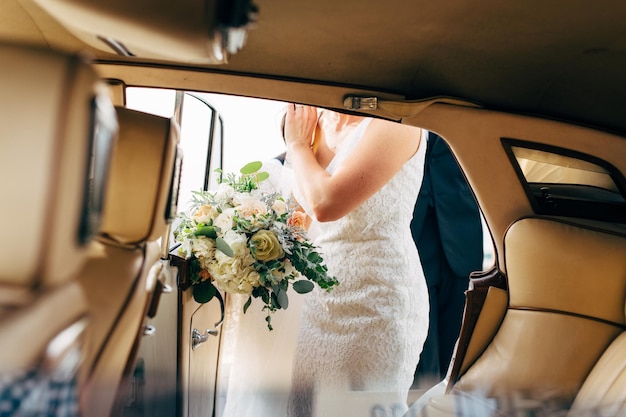 La moitié de la mariée avec un bouquet debout près de la voiture