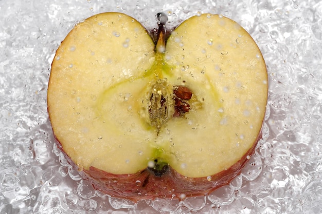 La moitié d'une pomme sucrée mûre rouge sur une plaque blanche est versée avec de l'eau d'une douche désinfectant la macrophotographie en gros plan