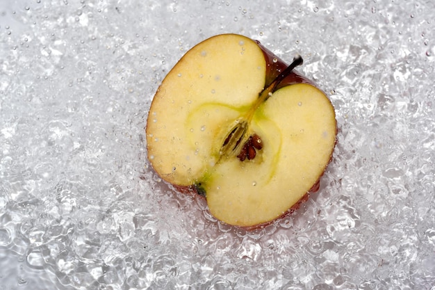 La moitié d'une pomme sucrée mûre rouge sur une plaque blanche est versée avec de l'eau d'une douche désinfectant la macrophotographie en gros plan