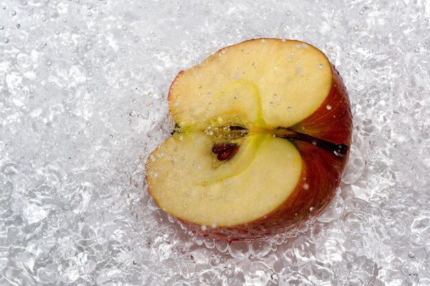 La moitié d'une pomme sucrée mûre rouge sur une plaque blanche est versée avec de l'eau d'une douche désinfectant la macrophotographie en gros plan