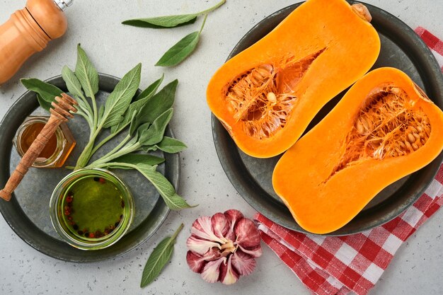 Moitiés de courge musquée biologique crue avec feuille de sauge, ail de poivre multicolore, miel, sel et poivre sur fond d'ardoise blanche, de pierre ou de béton. Fond de nourriture. Vue de dessus avec espace de copie.