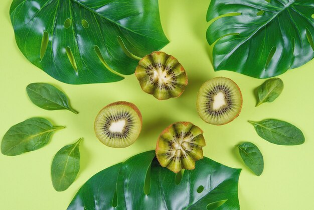 Moitiés de kiwi vert mûr, feuilles d'épinards et feuilles de monstera sur fond vert, vue de dessus, monochrome