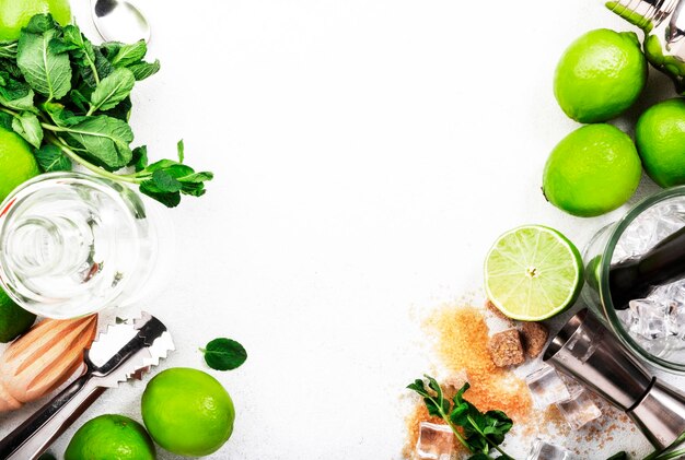 Mojito cocktail making Mint lime ice rhum blanc sucre de canne ingrédients et ustensiles de bar vue de dessus fond blanc mise à plat