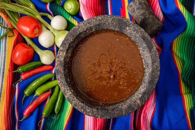 Molcajete avec sauce et légumes autour sur un serape coloré Ingrédients pour une sauce piquante