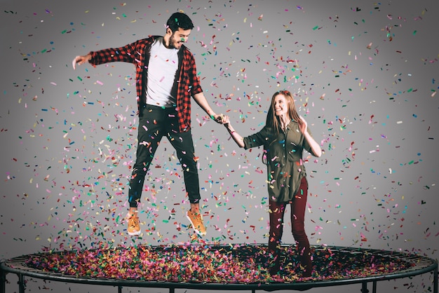 Moment amusant. Photo en l'air d'un beau jeune couple joyeux sautant sur un trampoline avec des confettis tout autour d'eux