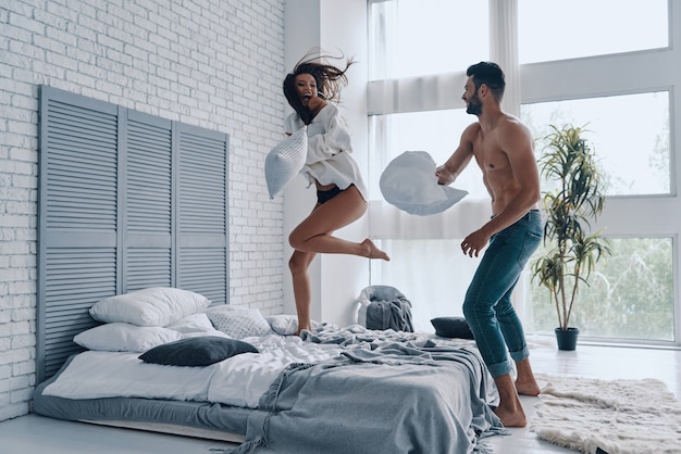 Moment amusant. Toute la longueur d'un jeune couple heureux s'amusant dans une bataille d'oreillers tout en passant du temps sans soucis dans la chambre