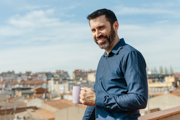 Moment de détente d'un homme d'âge moyen debout sur le balcon en train de boire du café