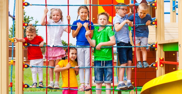 Moment ludique pour un groupe d'adorables enfants. Aire de jeux extérieure colorée avec filet de corde et échelle, beaucoup d'équipements pour les loisirs actifs