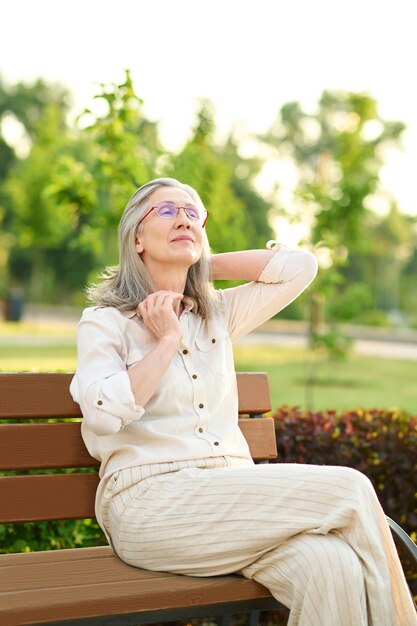 Moment de plaisir. Belle femme adulte avec des lunettes dans des vêtements légers se reposant de bonne humeur dans le parc par temps chaud