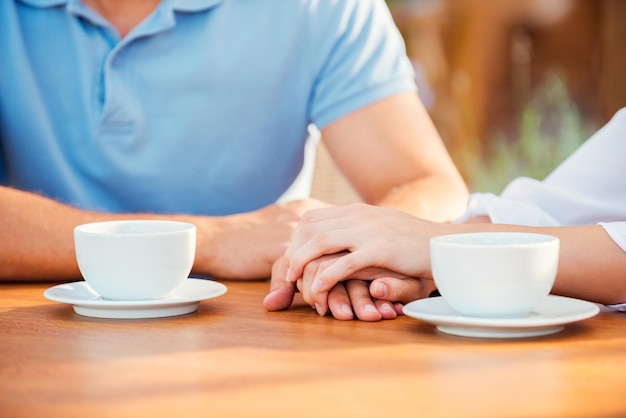 Moment romantique. Gros plan d'un couple se tenant la main alors qu'il était assis ensemble dans un café-terrasse avec des tasses à café sur la table