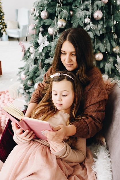 Moment tendre maman et fille avec livre près de l'arbre de Noël décoré