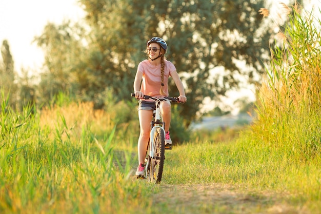 Moments Joyeuse jeune femme faisant du vélo au bord de la rivière et de la promenade des prés