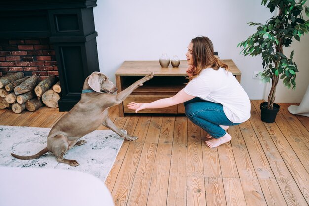 Moments de vie d'une jeune femme à la maison. Femme jouant avec son chien dans le salon